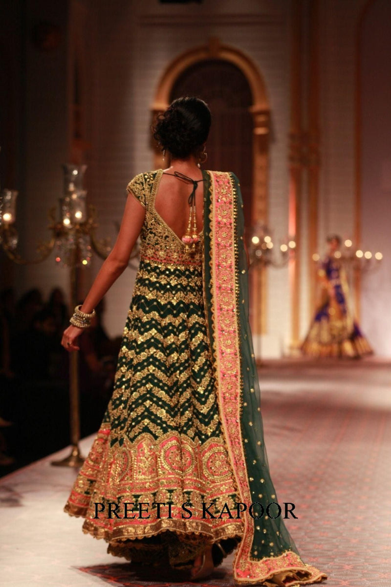 Woman in a green and gold traditional outfit walking on a runway with 'Priti S Kapoor' branding.