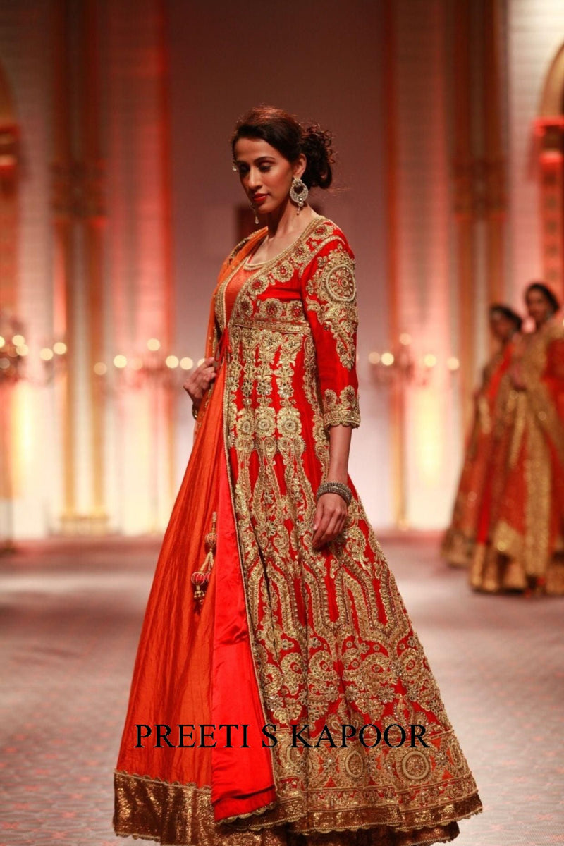 Woman in a red and gold traditional outfit on a stage with 'Preeti S Kapoor' branding.