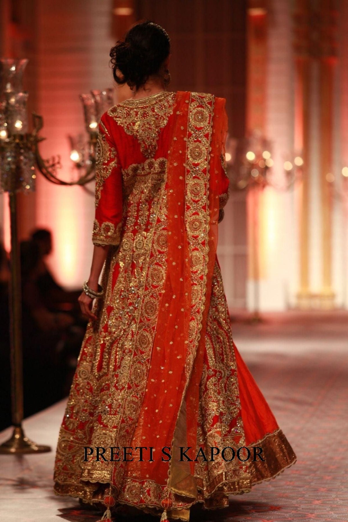 Red and gold embroidered traditional outfit on a model with 'Preeti S Kapoor' branding.