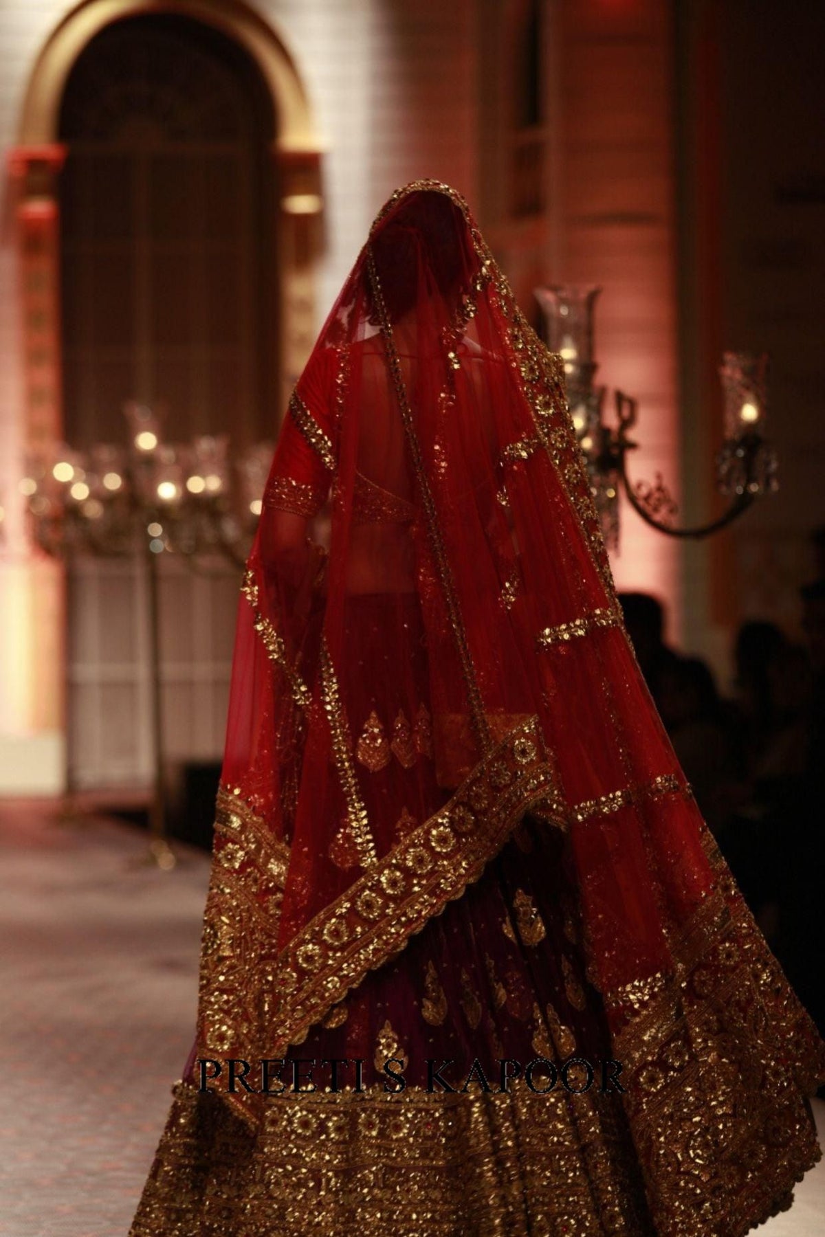 Red and gold embroidered traditional outfit with a veil in an indoor setting.
