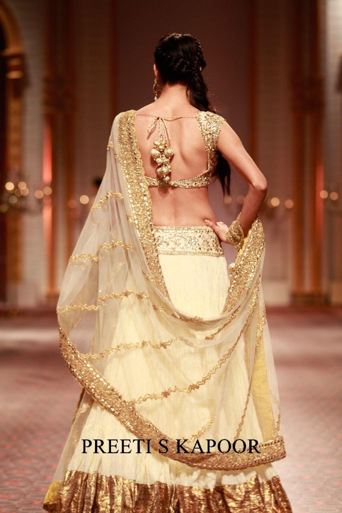 Woman in a gold and white saree with 'Preeti S Kapoor' branding in an indoor setting.