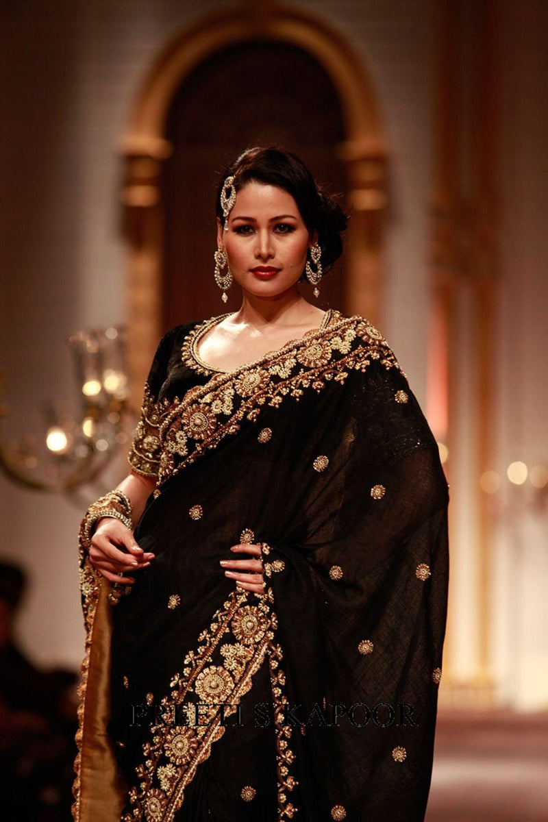Woman in a black saree with gold embroidery at an event.