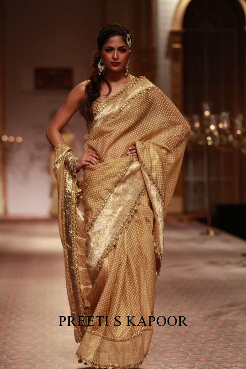 Woman in a gold saree with intricate patterns, walking on a runway. The brand 'Preeti S Kapoor' is visible.