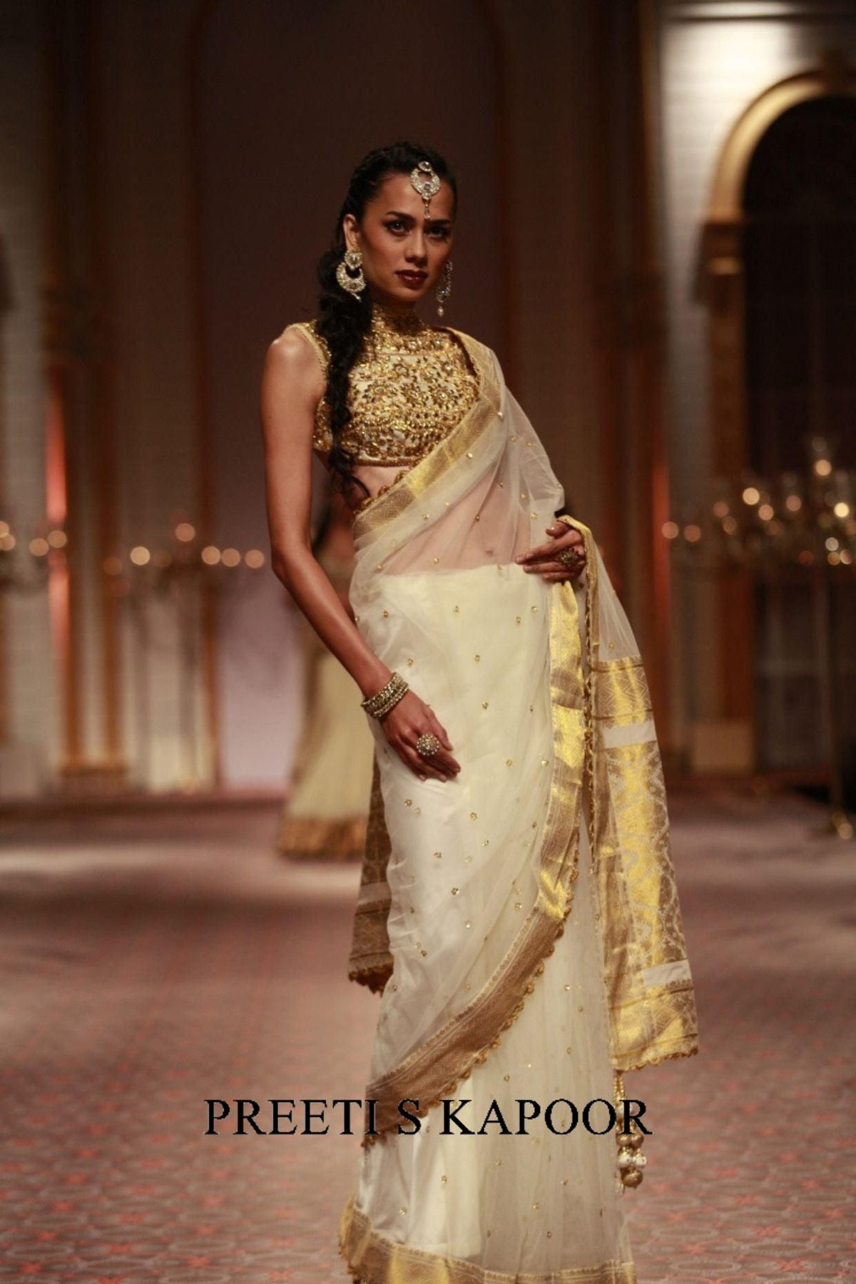 Woman in a traditional outfit with gold and white colors, standing indoors.