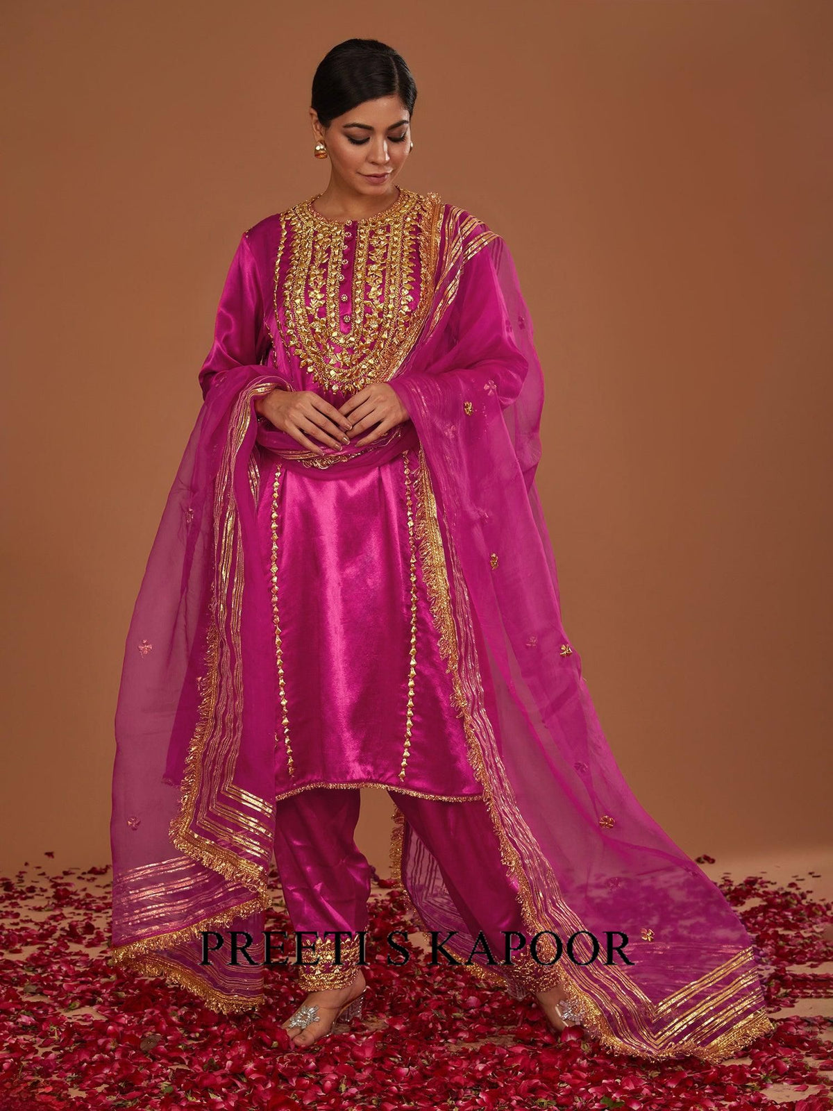 Woman in a pink traditional outfit with gold embroidery on a brown background