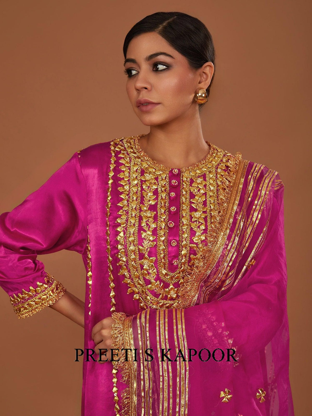 Woman wearing a pink traditional outfit with gold embroidery against a brown background