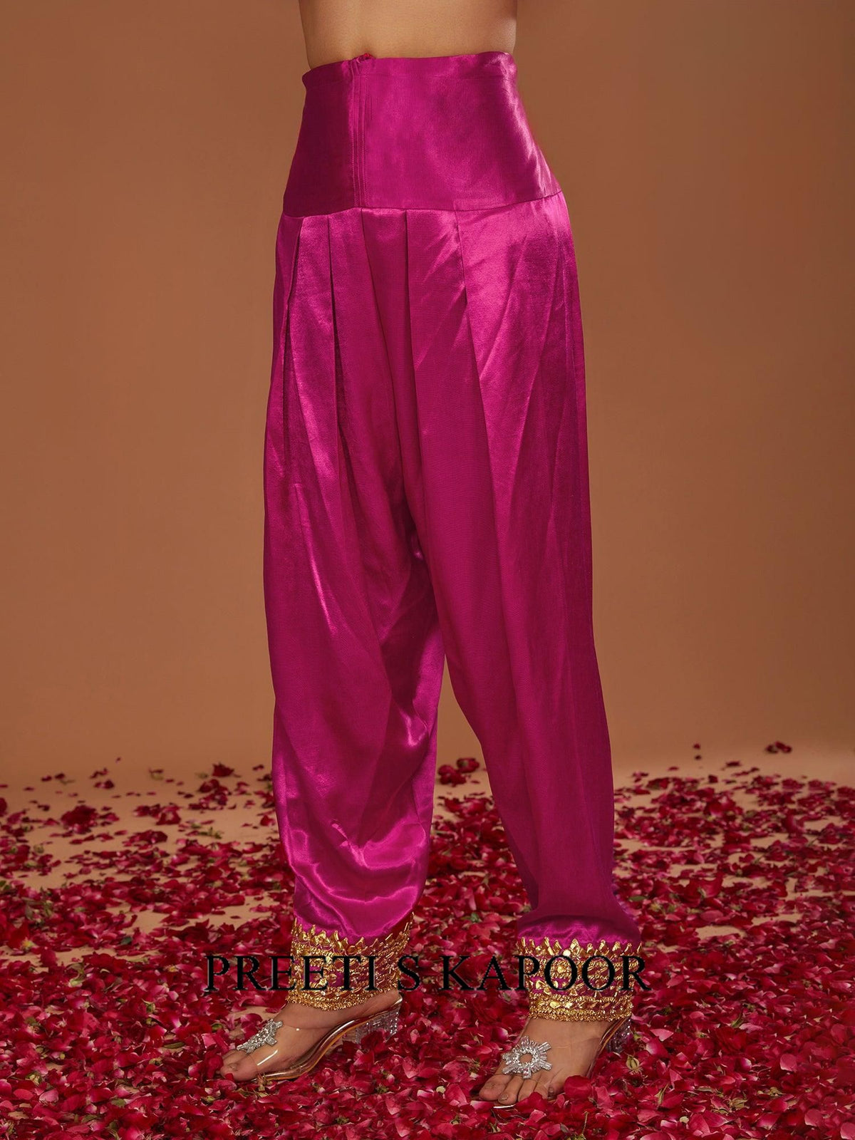 Pink satin pants with gold sandals on a brown background