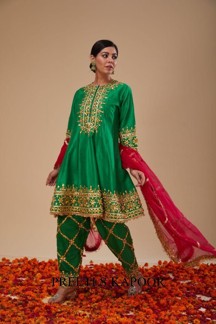 Woman in a green embroidered outfit with red dupatta on a beige background