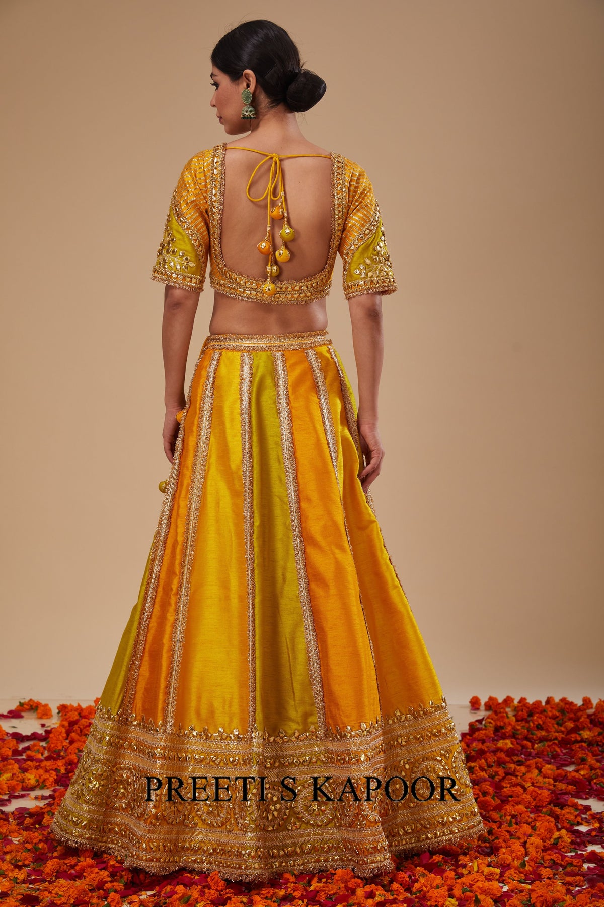 Woman wearing a yellow and gold traditional outfit with 'Preetis Kapoor' branding.