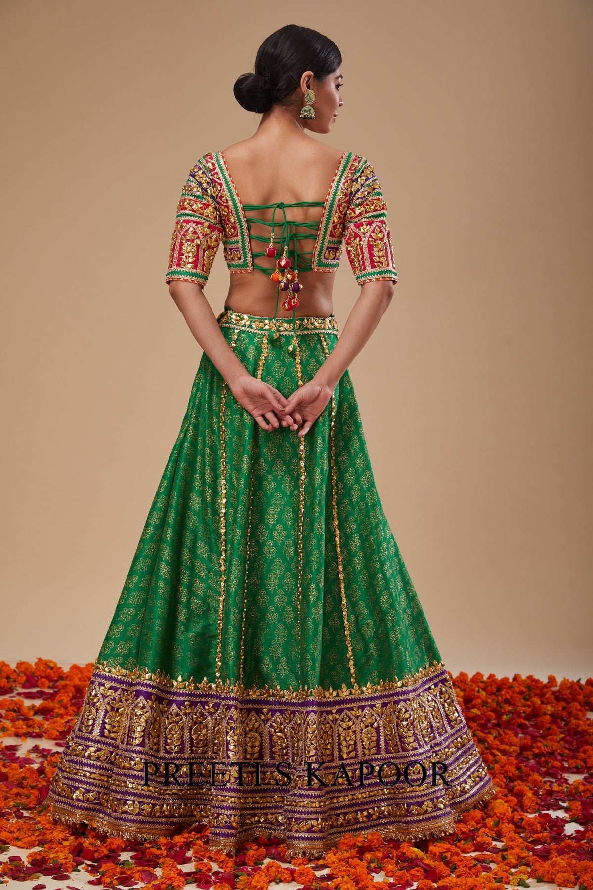 Woman wearing a green embroidered traditional outfit with 'Kleek' branding on a beige background.