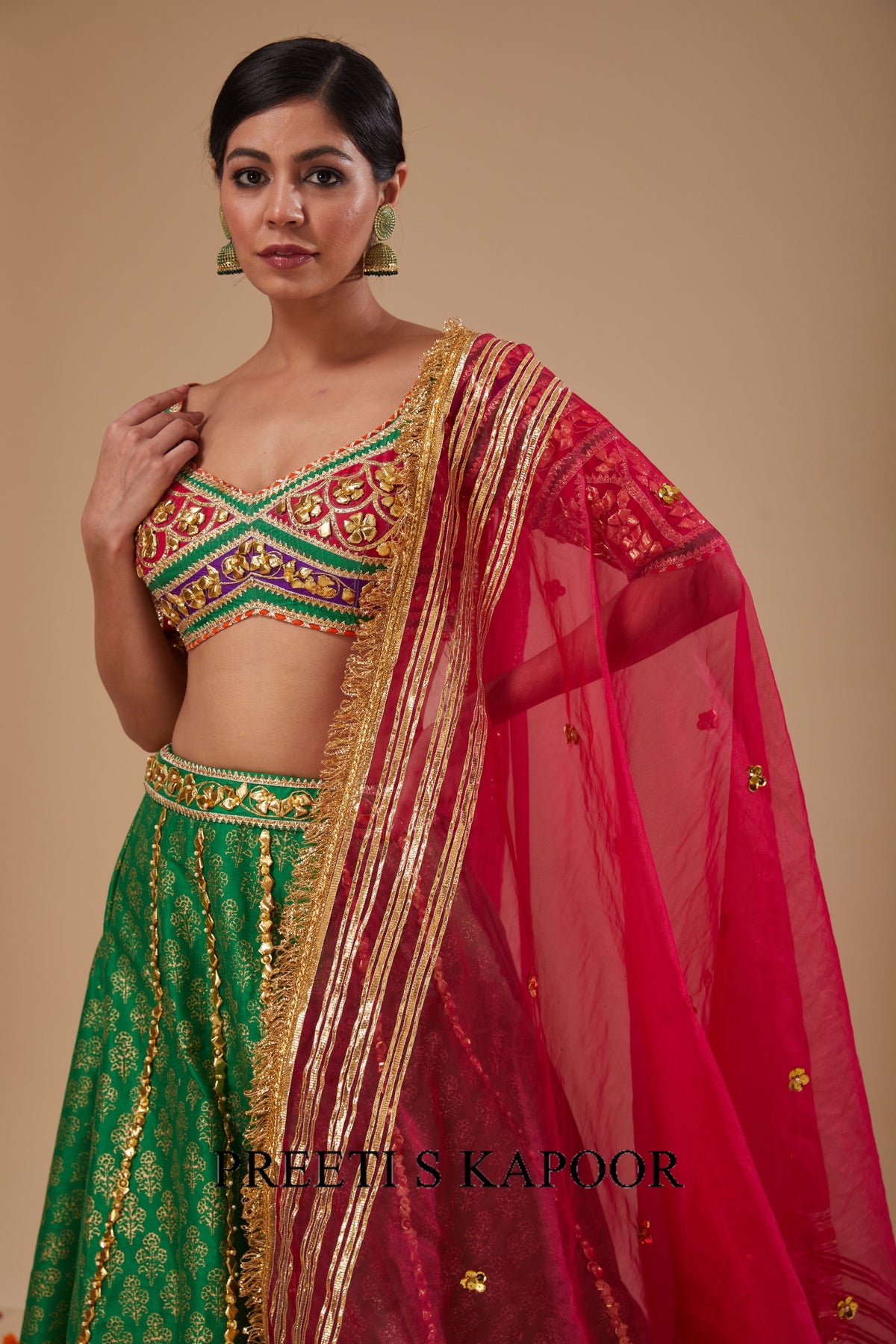 Woman wearing a green and red traditional outfit with gold detailing on a beige background