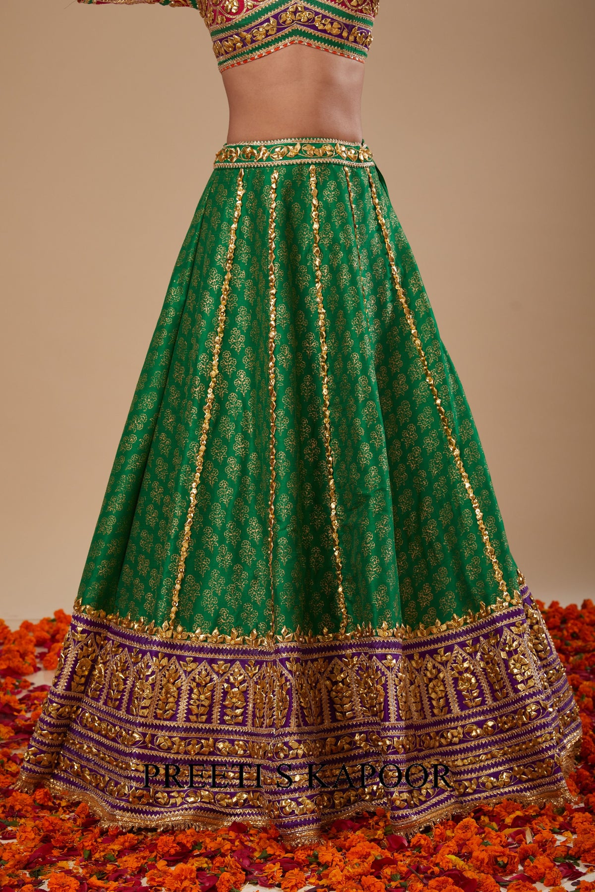 Green embroidered traditional outfit with gold details on a beige background
