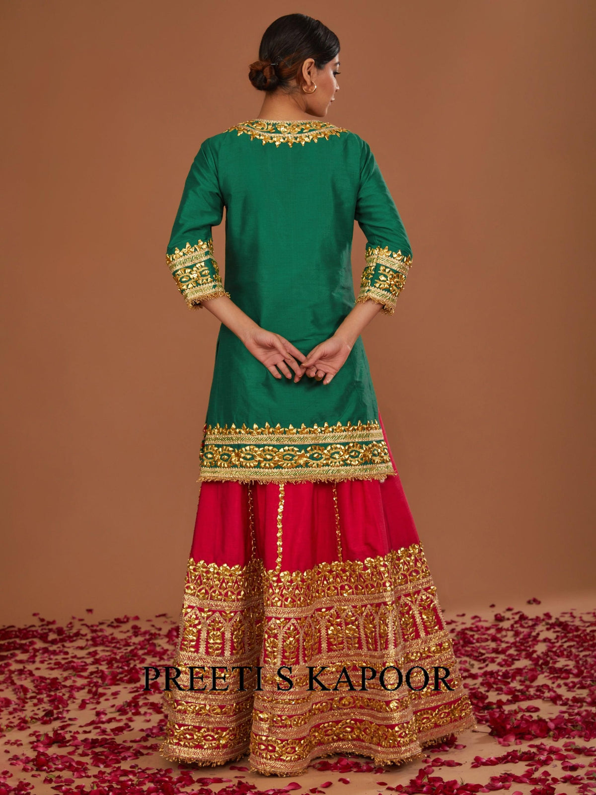 Woman wearing a green and red traditional outfit with gold embroidery on a brown background.