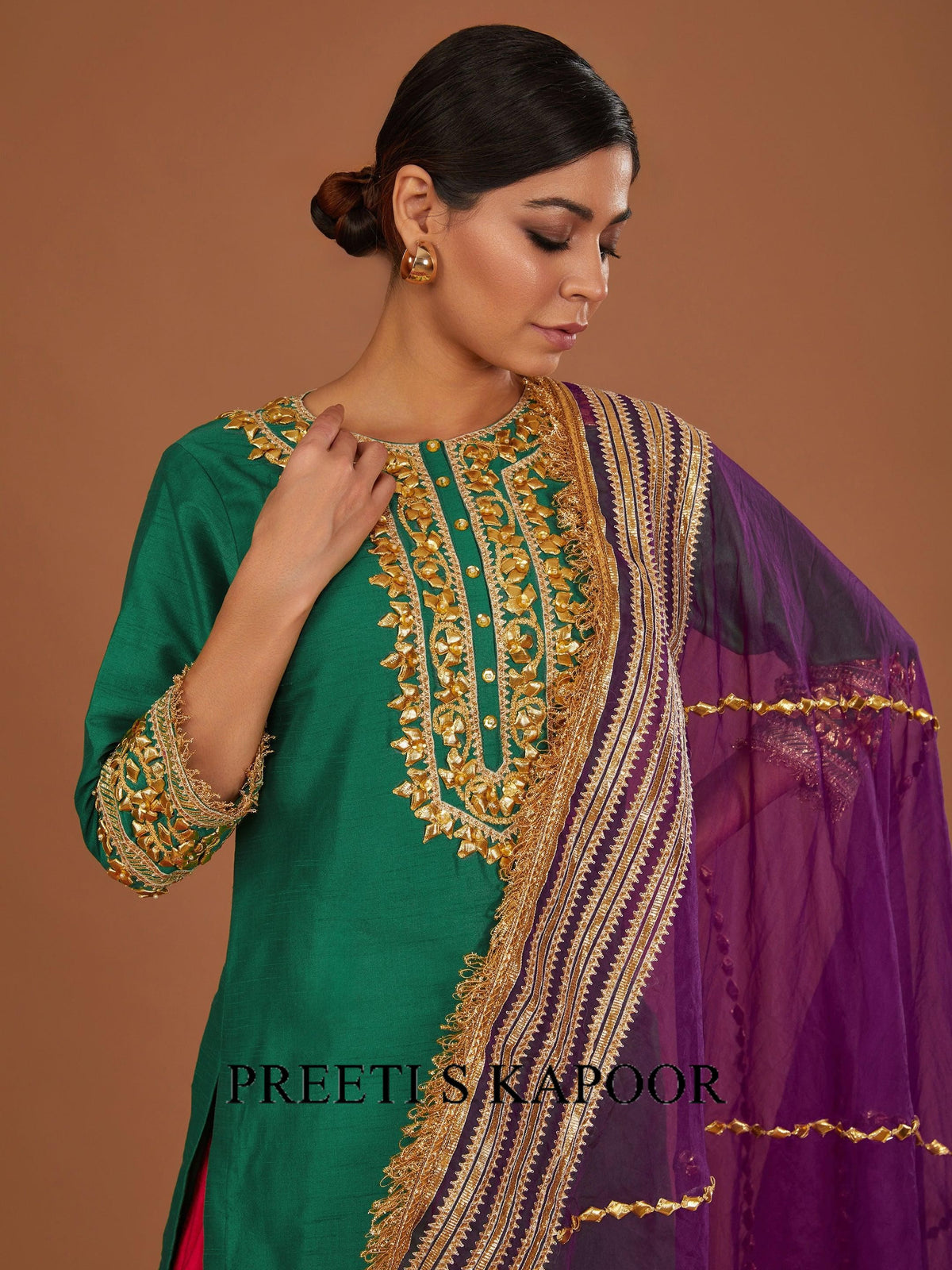 Woman wearing a green and purple embroidered traditional outfit with 'Preetis Kapoor' branding.