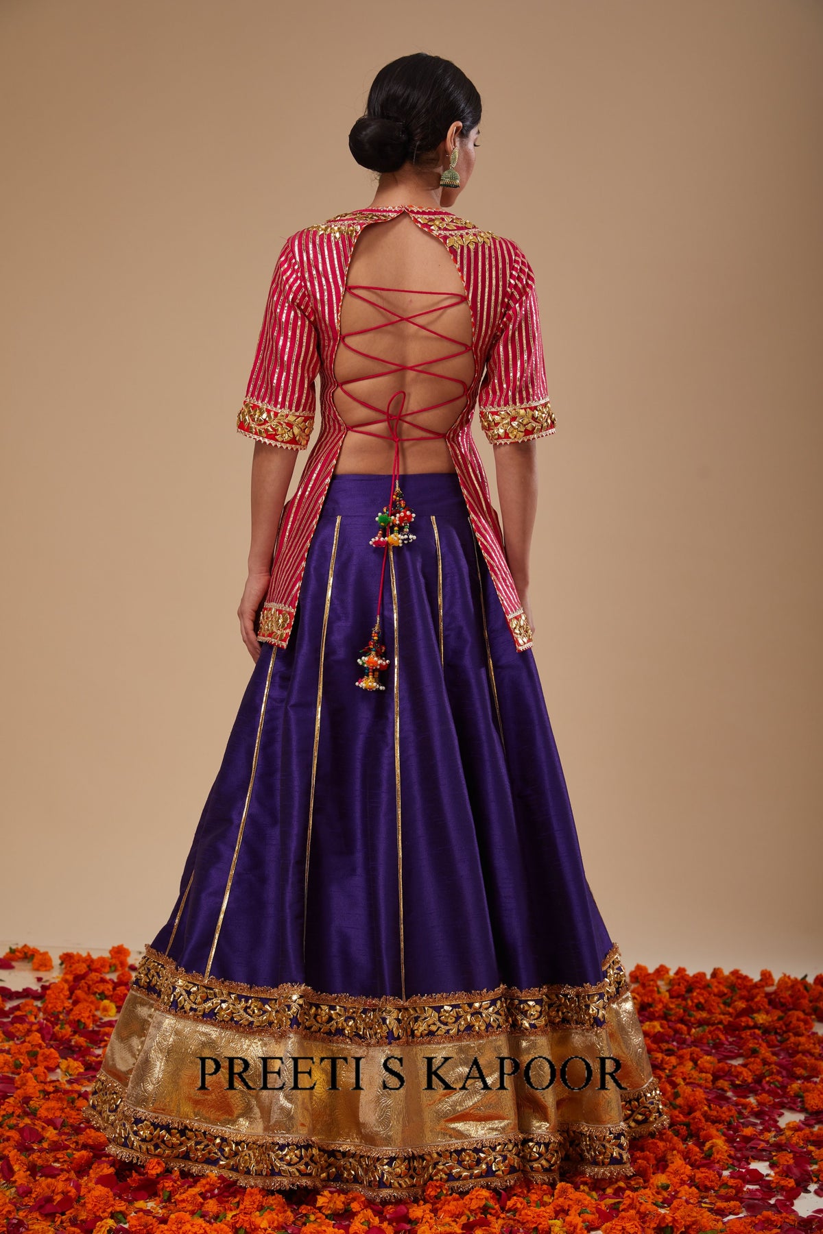 Traditional Indian outfit with a purple skirt and red blouse on a beige background.