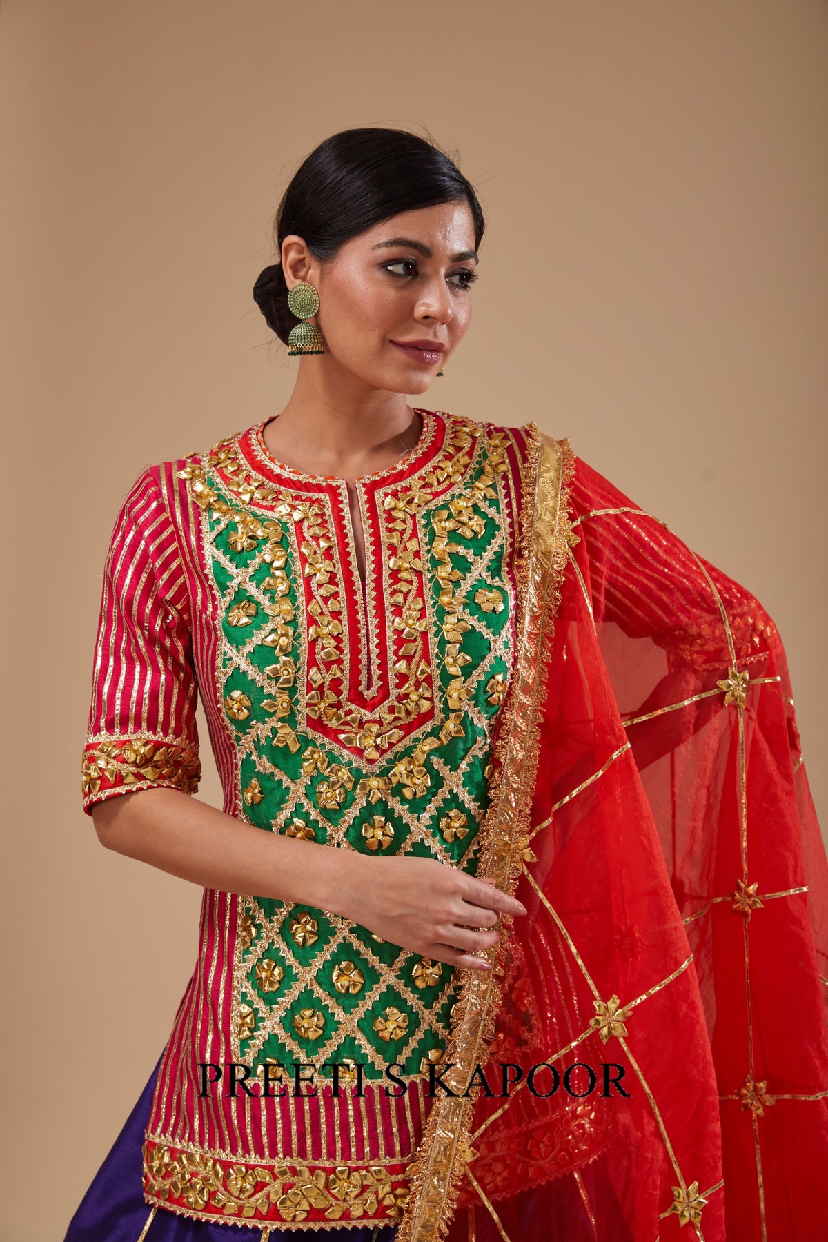 Woman wearing a traditional embroidered outfit with a red dupatta against a beige background