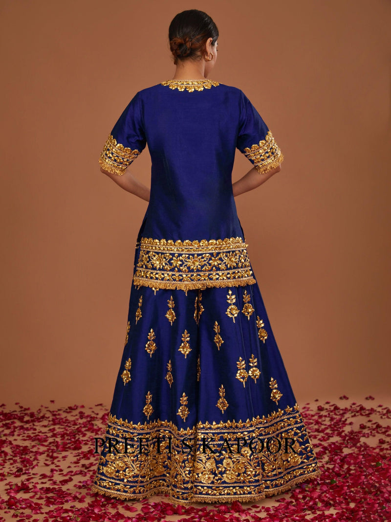 Woman wearing a blue traditional outfit with gold embroidery on a brown background