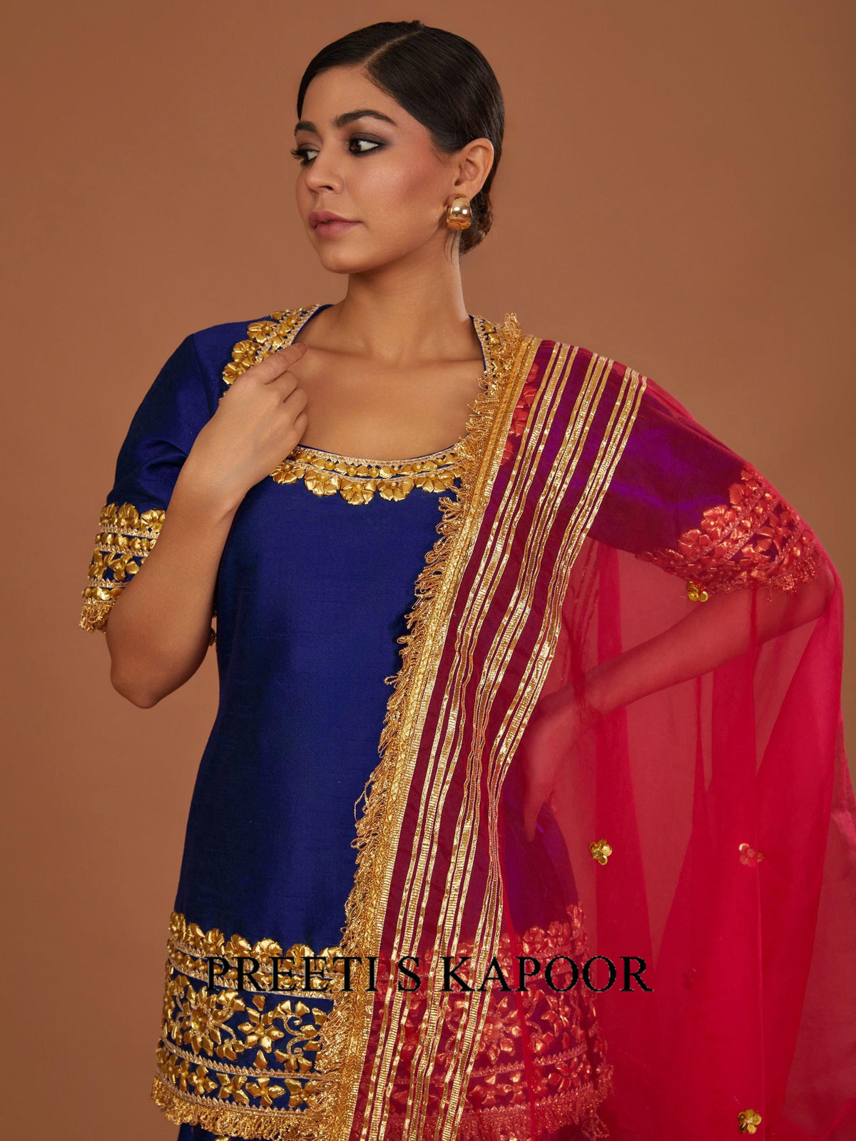 Woman wearing a traditional blue and red saree with gold border, branded 'Preeti S. Kapoor'.