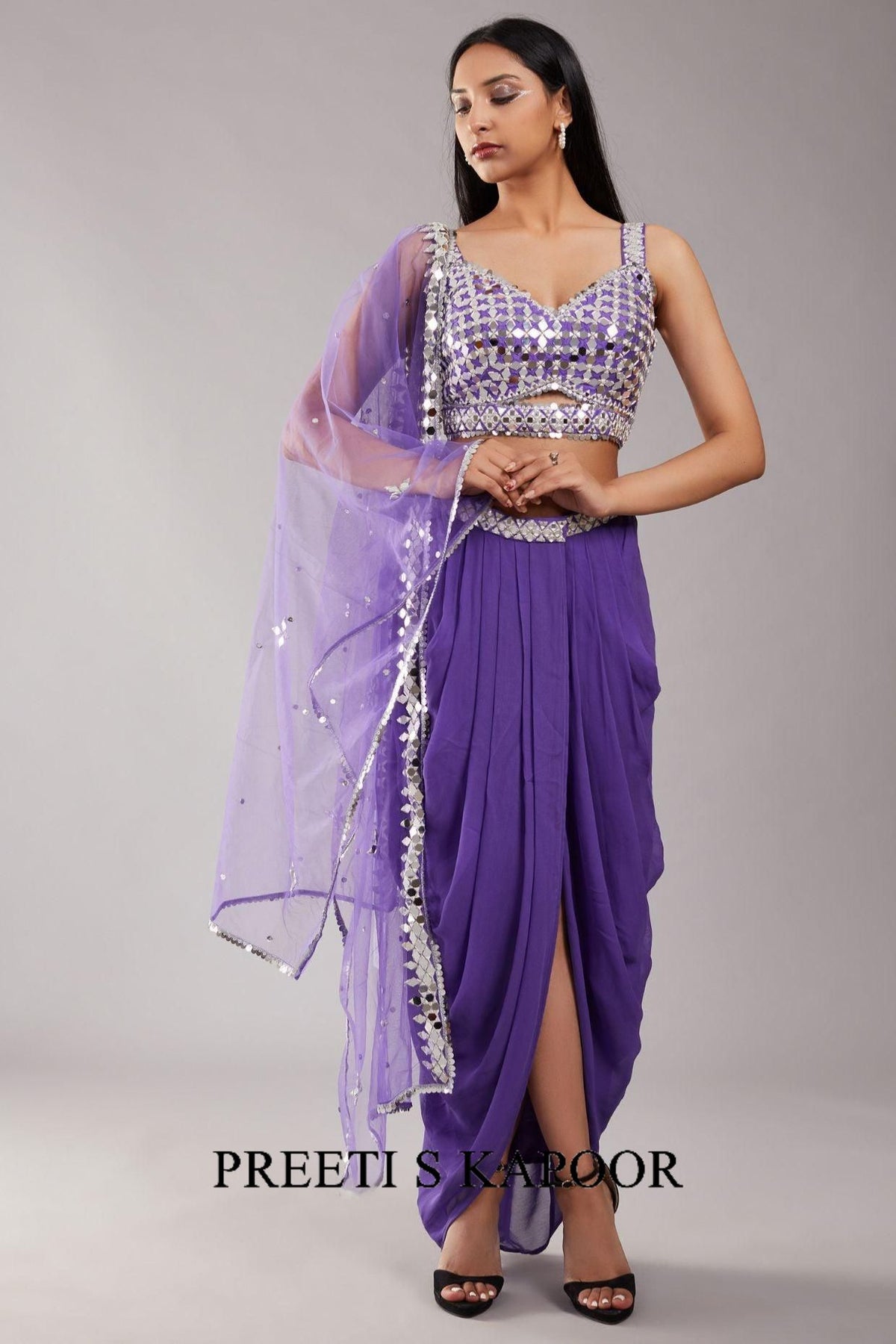 Woman wearing a purple saree with silver embellishments on a gray background, branded 'Preeti S Kapoor'.