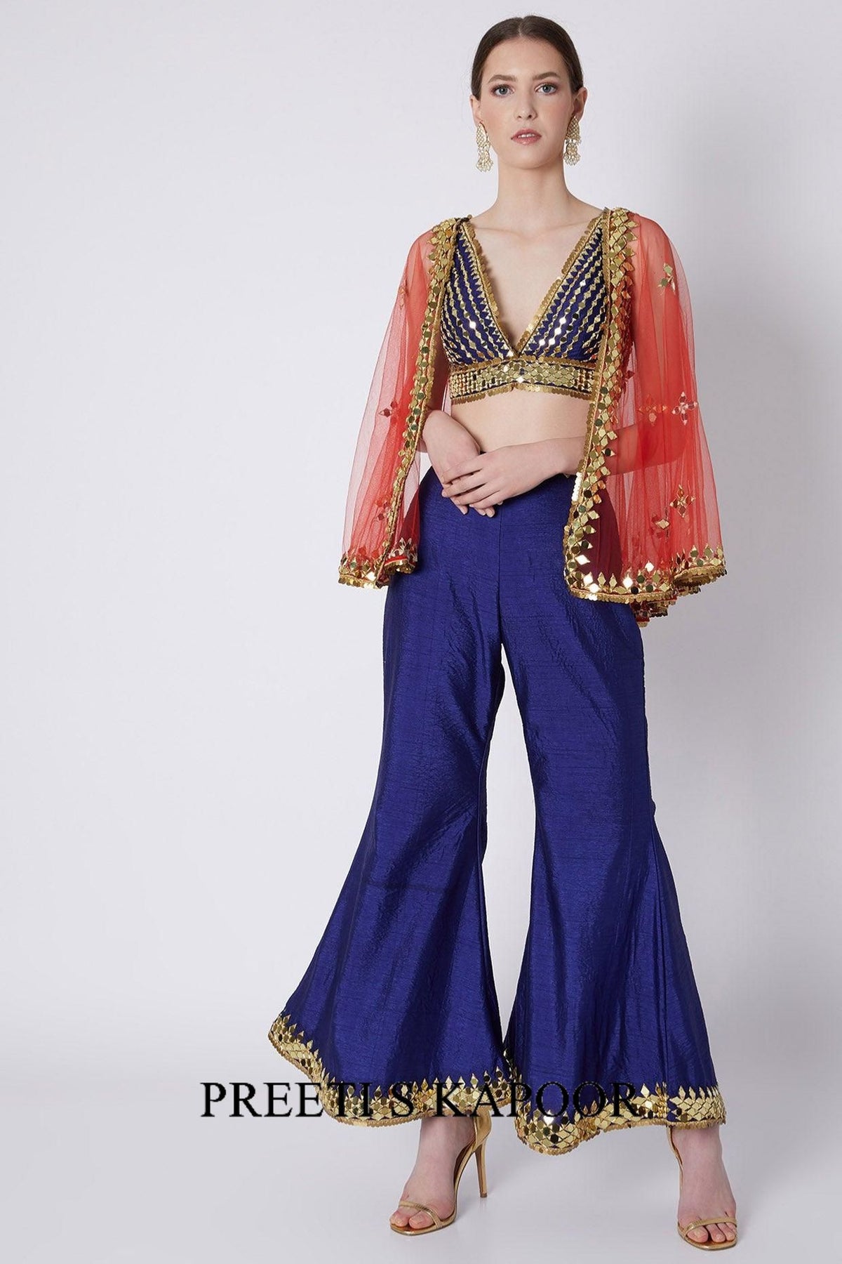 Woman wearing a traditional outfit with a red blouse, blue saree, and gold embroidery on a white background.