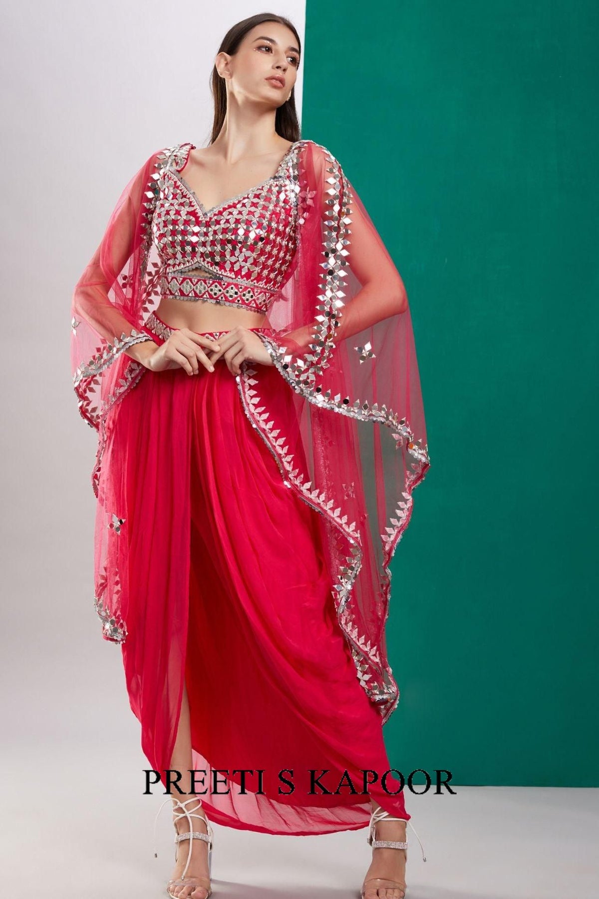 Woman wearing a red saree with silver embellishments against a green background, branded 'Preeti S Kapoor'.