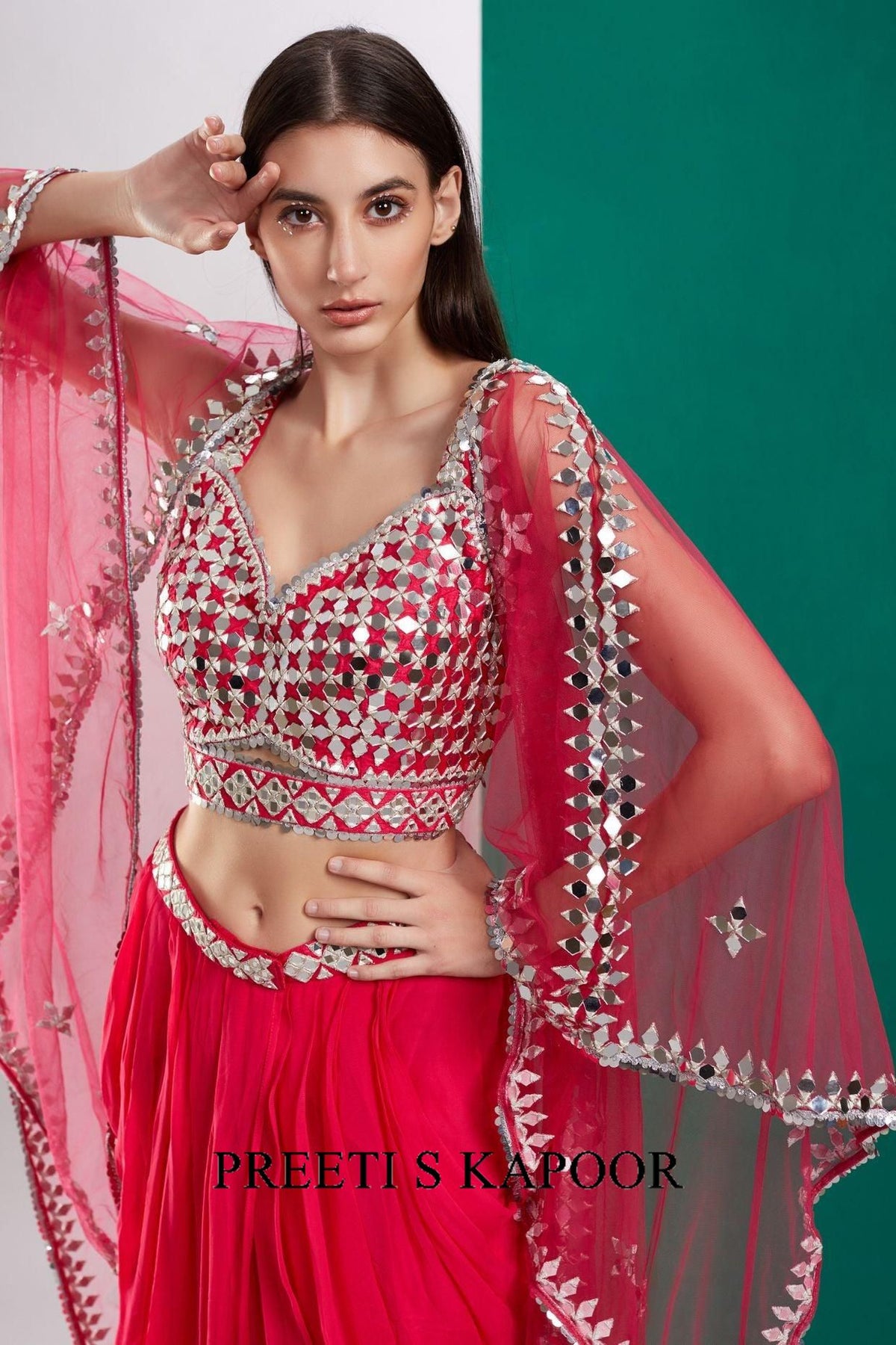 Woman wearing a red and silver traditional outfit with a pink dupatta, branded 'Preeti S Kapoor'.