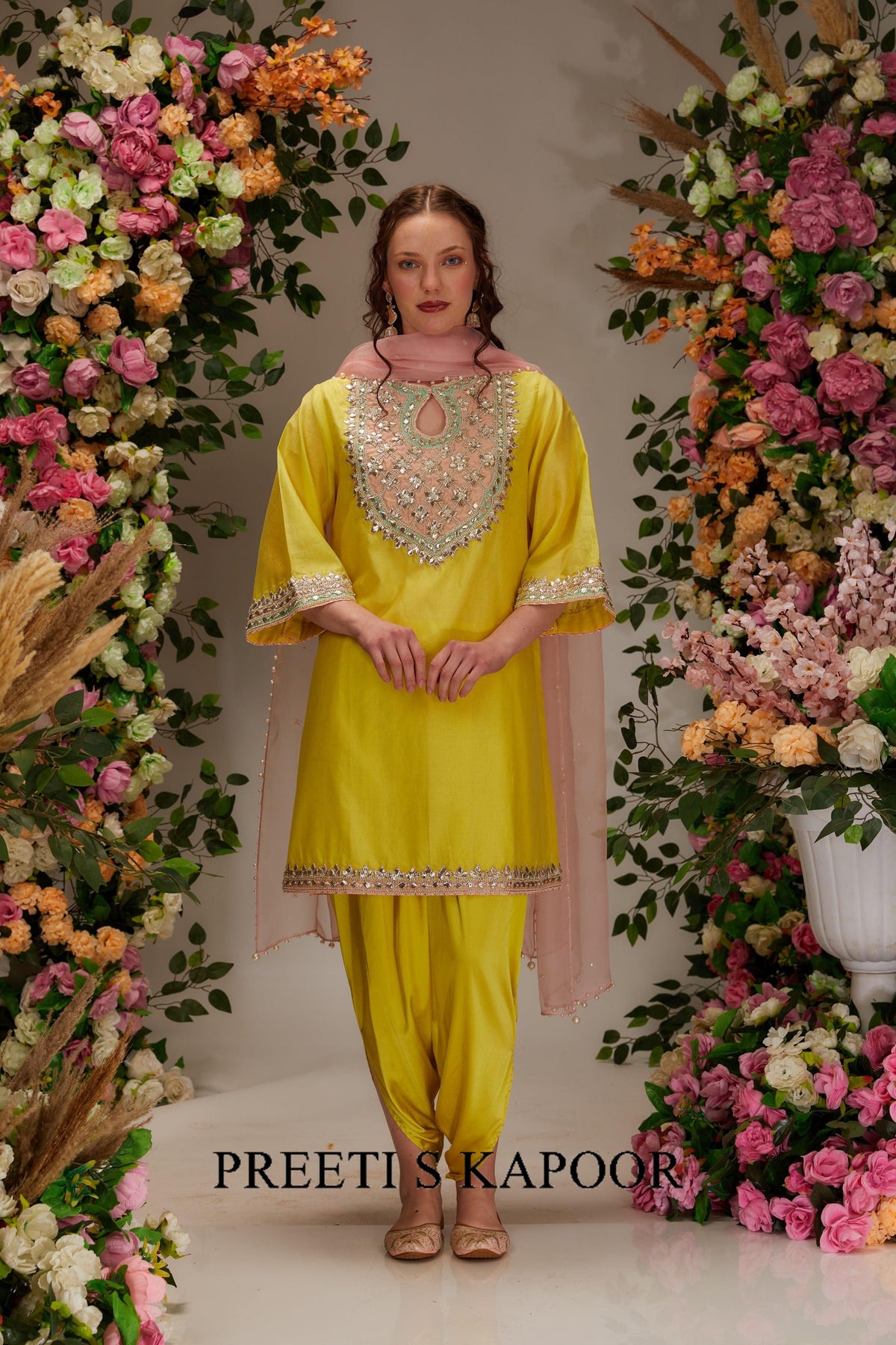 Woman in a yellow traditional outfit with floral decorations on either side.
