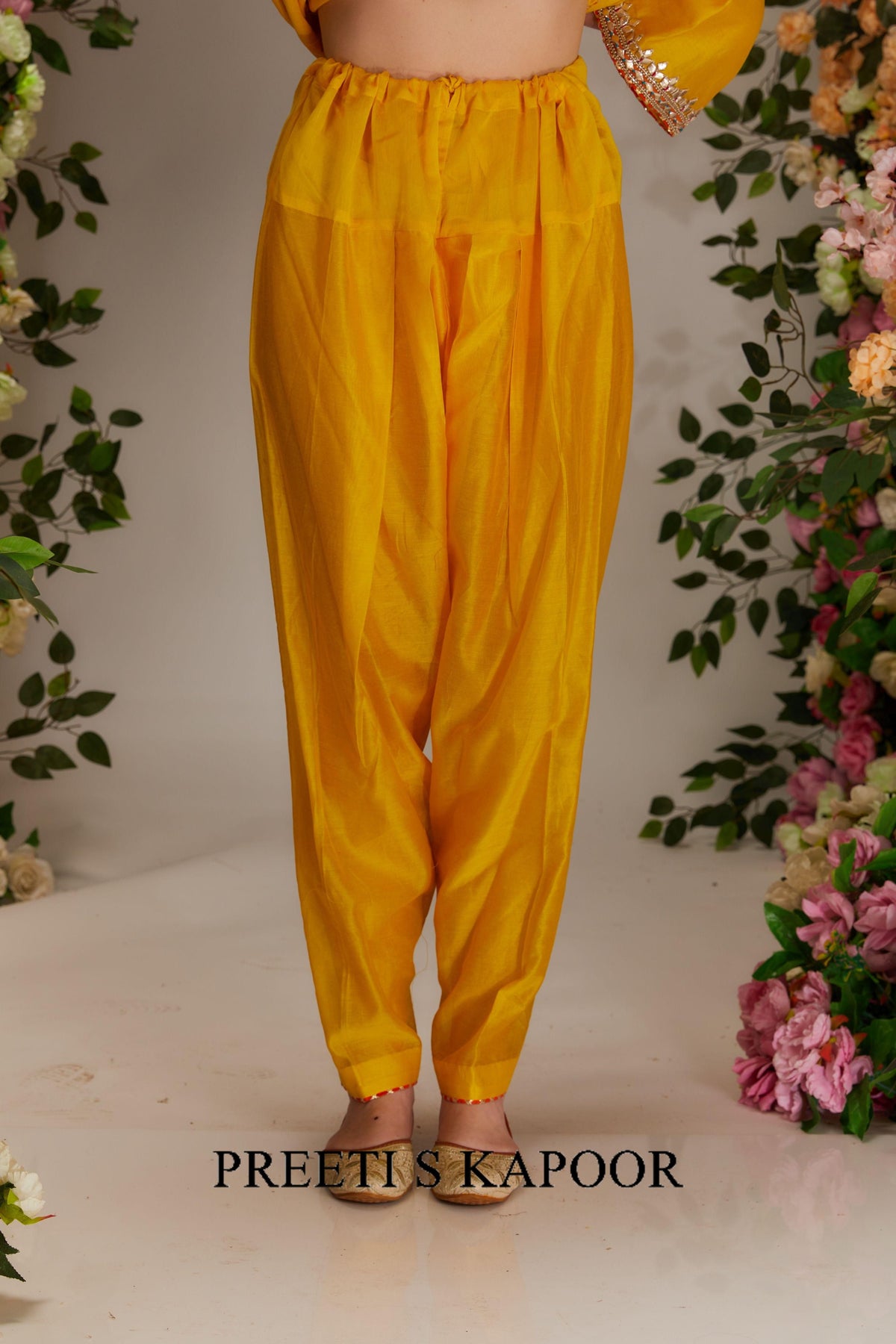 Yellow pants worn by a person with floral decorations on a light background, featuring the brand 'Preeti S Kapoor'.